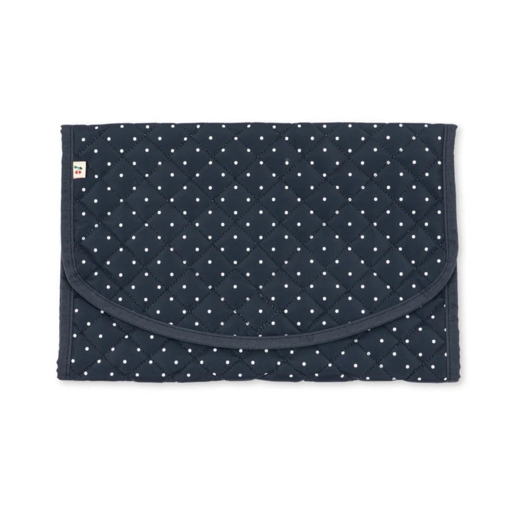 A navy blue quilted baby blanket with a white polka dot pattern, featuring a curved front pocket and a small white tag on the left side, shown flat against a white background.