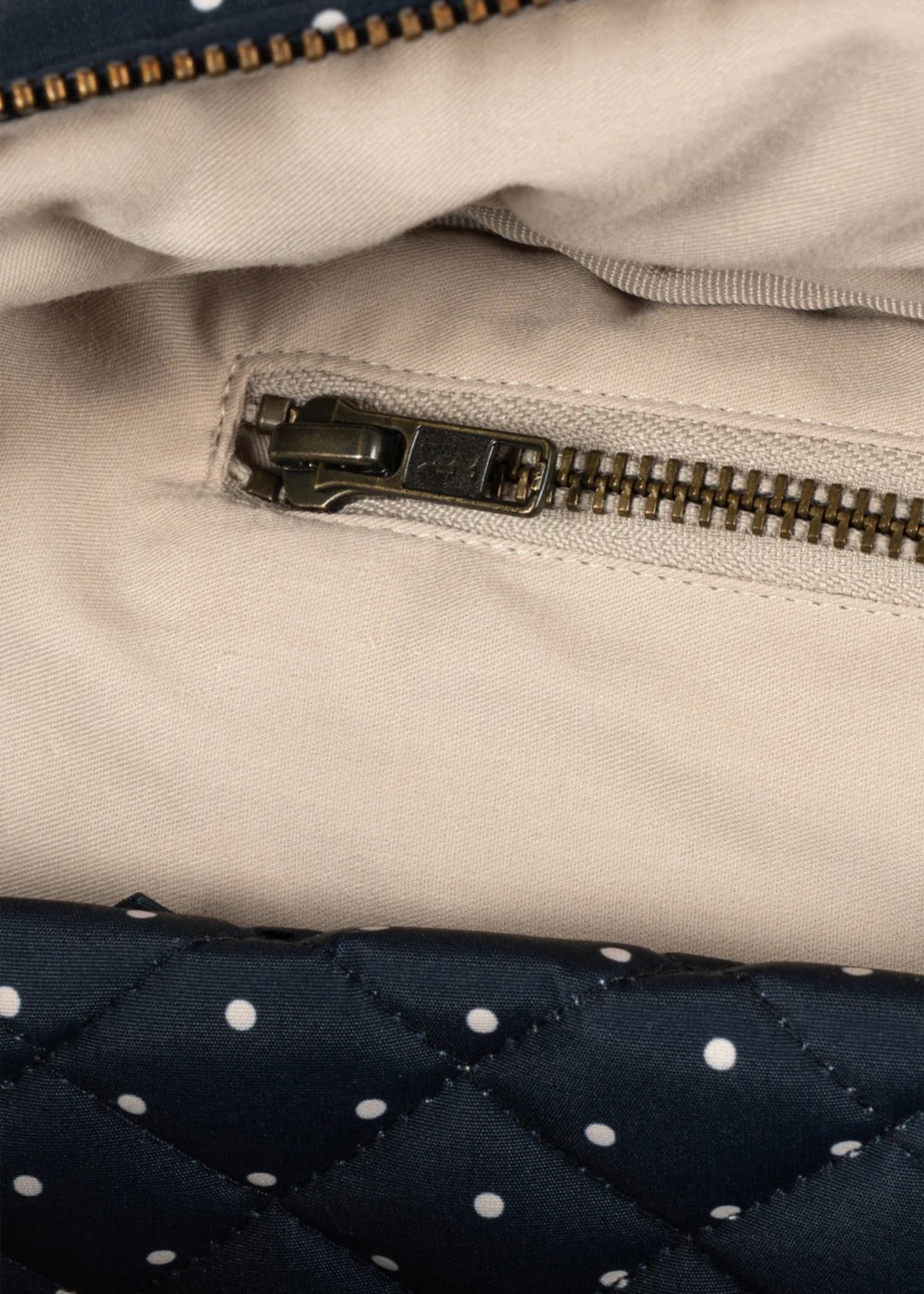 Close-up detail of a quilted navy blue bag with white polka dots and a gold zipper, next to a beige fabric panel with a dark metal zipper.