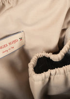 Close-up of a beige garment with gathered elastic trim and a sewn-in fabric label reading "NGES SLOJD" and "cherry on tap."
