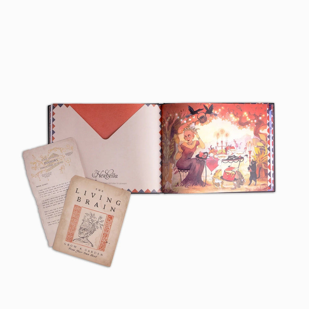 An open illustrated book or album with a warm-toned fantasy scene on the right page and printed cards or inserts placed in front, photographed on a clean white background.