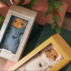 Two LIEWOOD MINNIE dolls in plush animal suits displayed in their decorative window boxes, surrounded by gift boxes and evergreen branches.