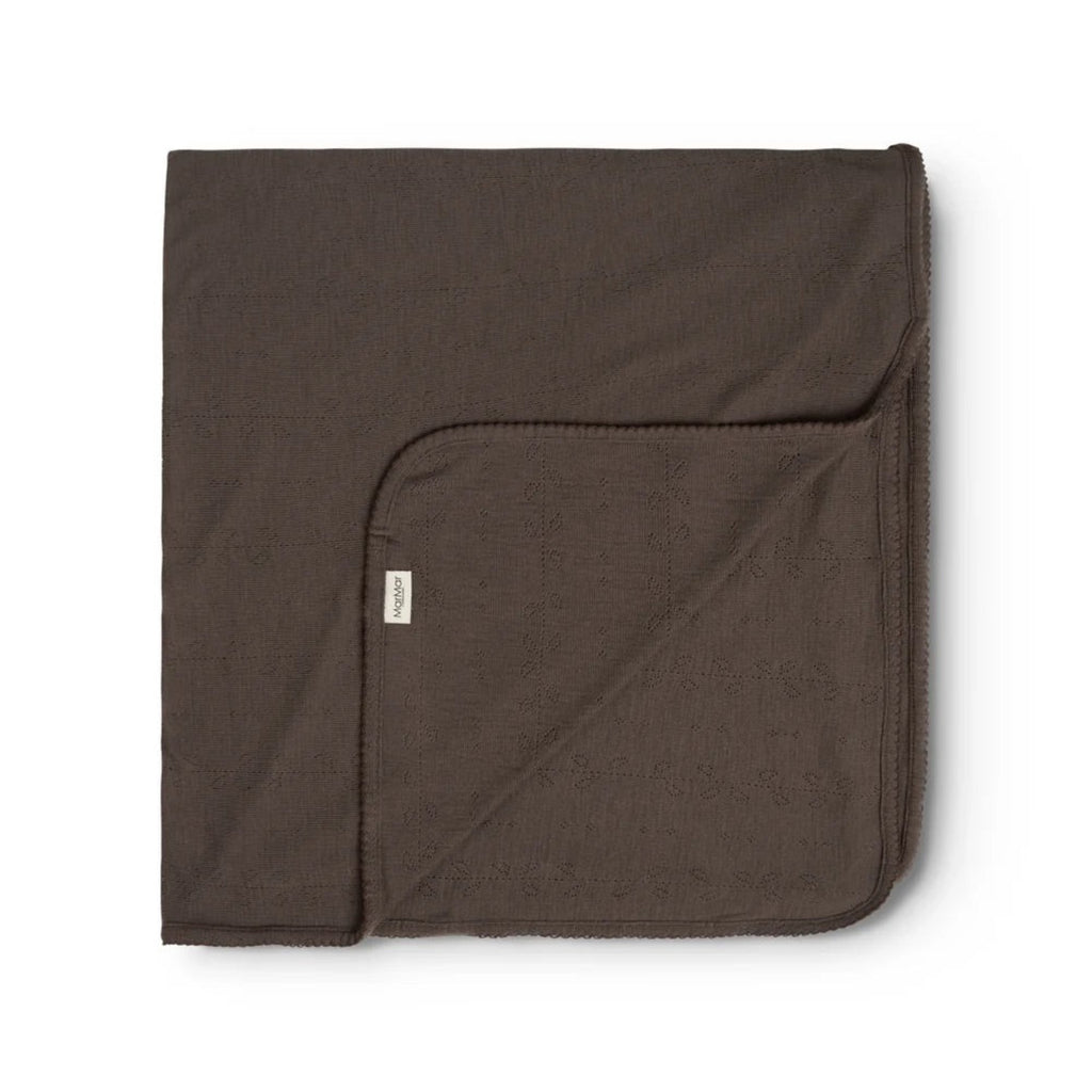 A folded dark brown cotton blanket with a small white brand tag, displayed on a clean white background.