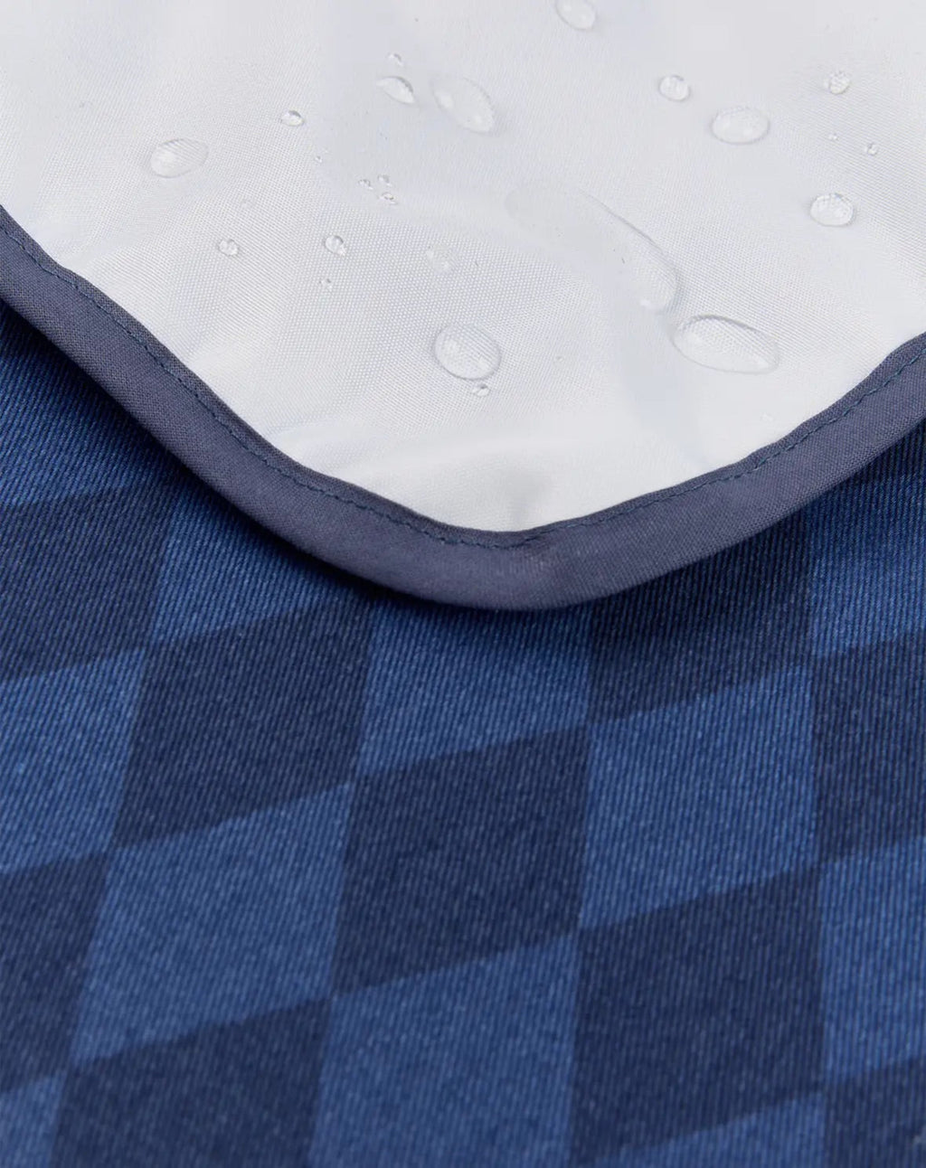 Close-up of a blue and navy checkered fabric surface with a white padded section showing water droplets on top.