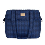 A navy blue quilted diaper bag with a subtle diamond pattern, featuring a tan leather brand patch on the front, set against a plain white background.