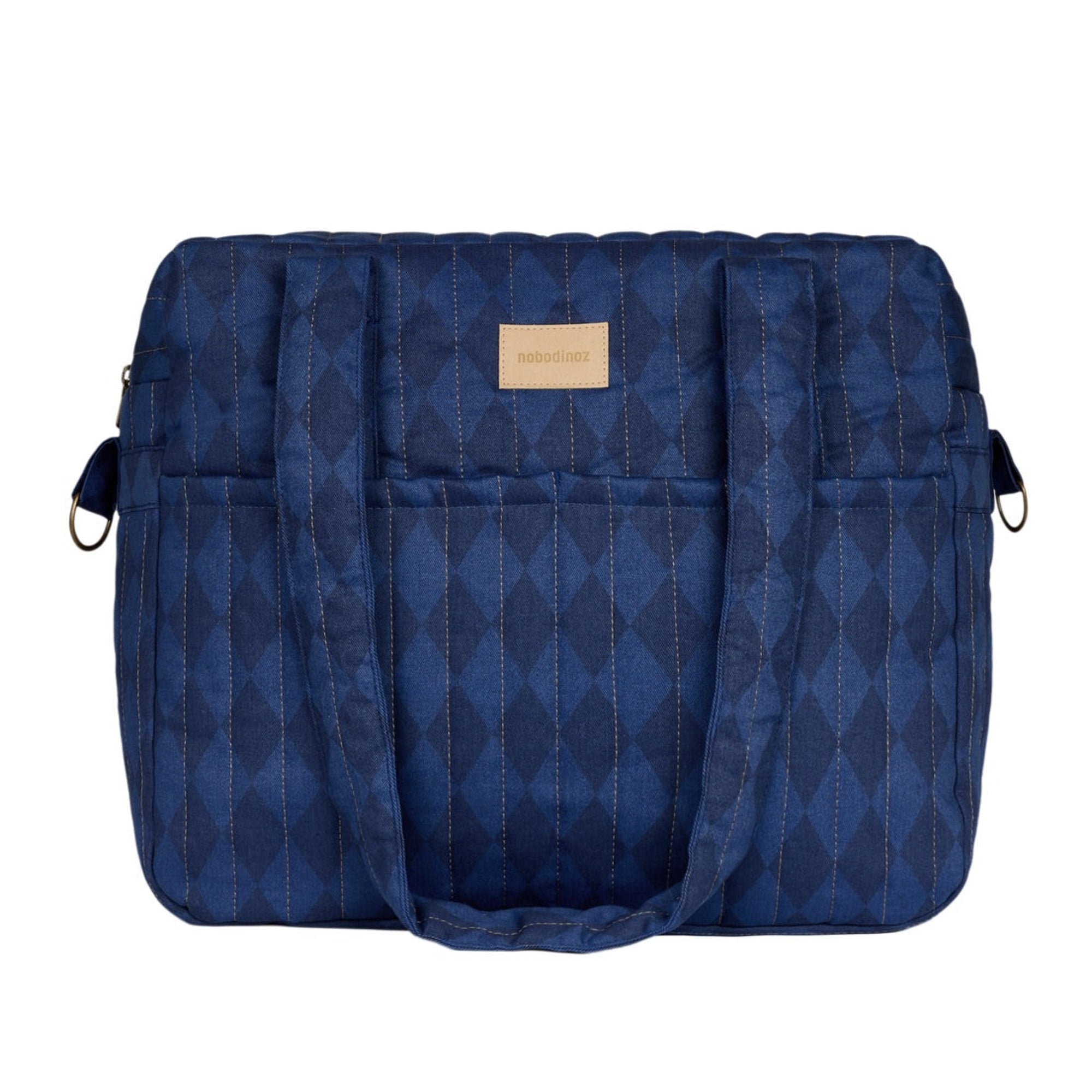 A navy blue quilted diaper bag with a subtle diamond pattern, featuring a tan leather brand patch on the front, set against a plain white background.