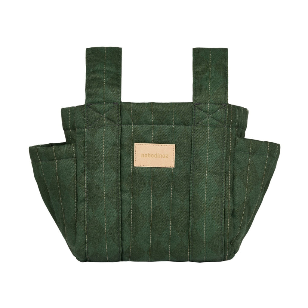 A dark green quilted fabric tote bag with vertical stitching, dual shoulder straps, and a small tan leather brand patch on the front, shown against a plain white background.